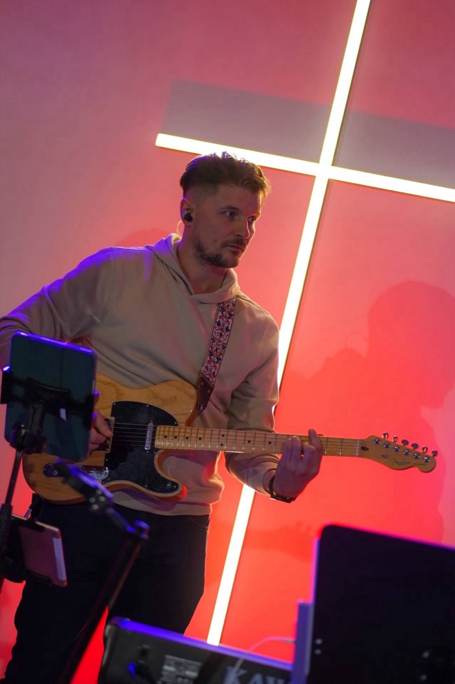 Kamil gra na gitarze na scenie, za nim podświetlony krzyż